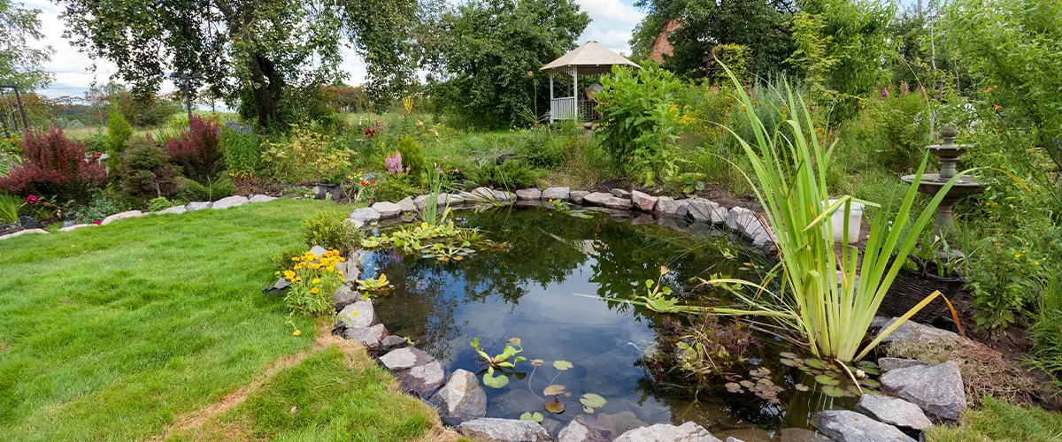 Beautiful garden pond surrounded by lush greenery, colorful flowers, and a peaceful gazebo, creating a serene backyard oasis.