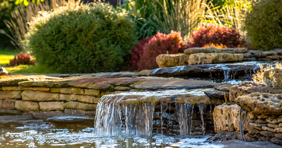 Small cascading water feature in a garden pond with stone walls and lush green plants