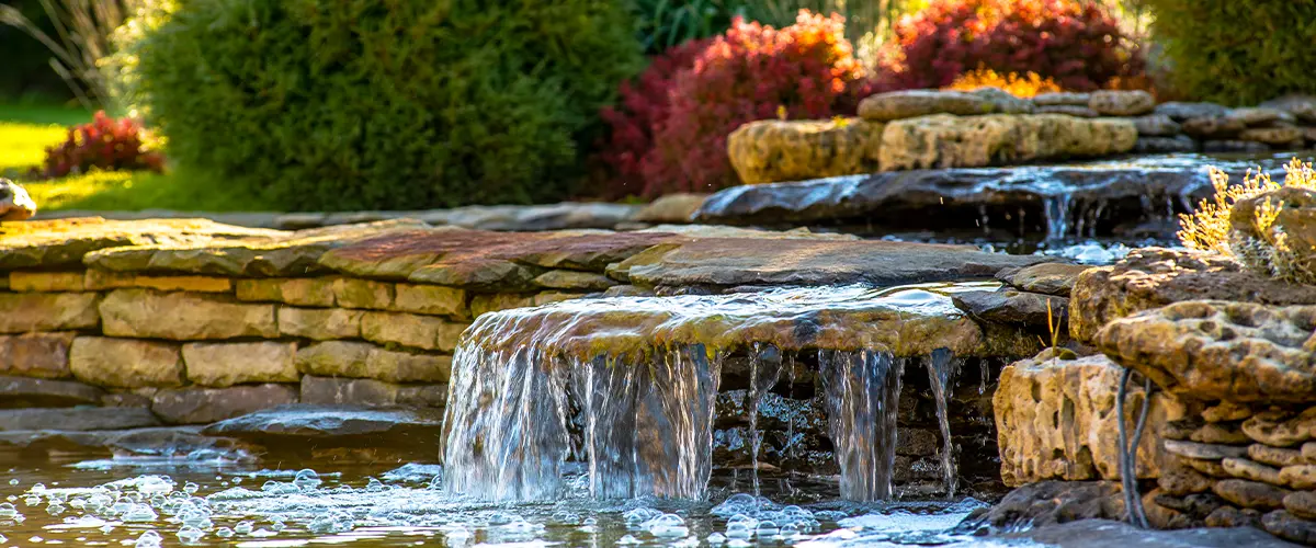 Small cascading water feature in a garden pond with stone walls and lush green plants