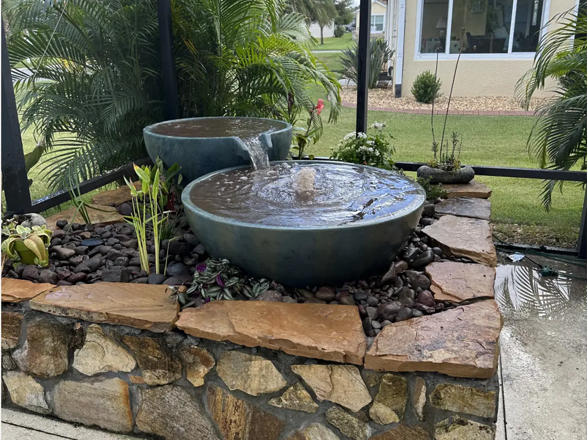 Finished indoor stone fountain with two water bowls, decorative rocks, and surrounding greenery for a tranquil setup.