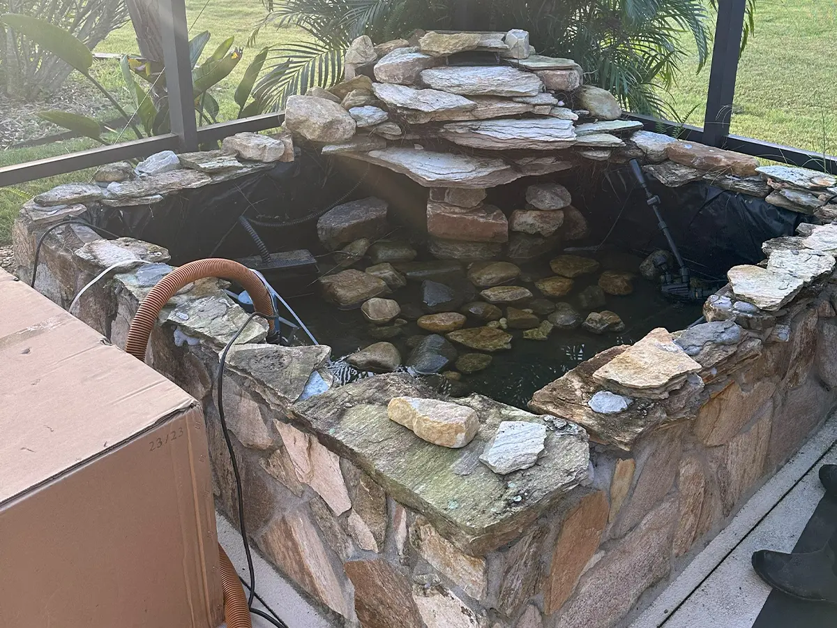 Stone pond under construction with rocks and tubing for a custom indoor fountain installation.