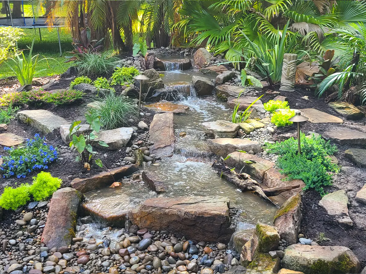 Natural pondless waterfall installation with lush greenery and cascading water, enhancing backyard landscape aesthetics.