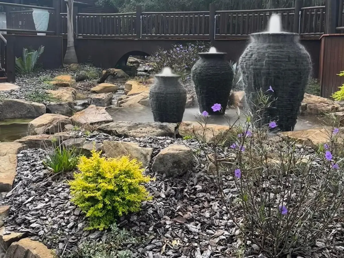 Garden fountain with cascading water urns surrounded by rocks and purple flowering plants