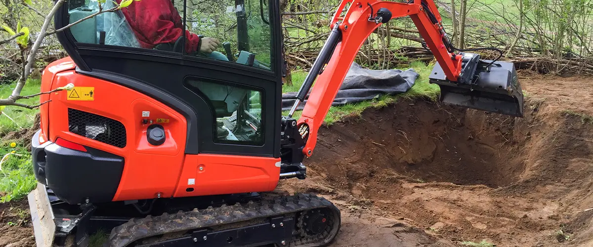 Mini excavator digging a hole in a backyard, preparing the ground for landscaping or pond installation.